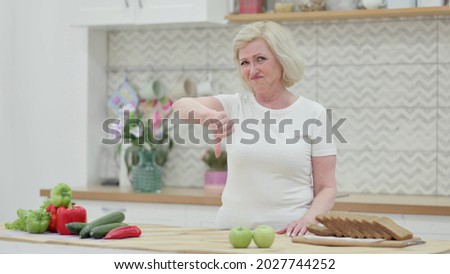 Old Woman Showing Thumbs Down while Standing in Kitchen