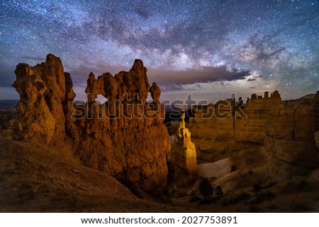 A hoodoo with small windows and Thor's Hammer against a night sky with clouds and the Milky Way below Sunset Point in ryce Canyon National Park, Utah.