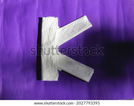 Letter K of white tissue isolated on purple background. The concept of natural light and shadow.