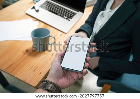Closeup image of man hand passing mobile with blank screen to his partnership while working in office.