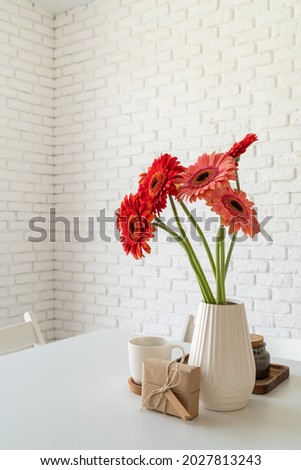 Happy birthday gerbera daisy flowers in a vase with a craft gift box on white kitchen table, minimal style