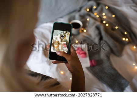 Woman making picture on smart phone of winter cozy home interior over Christmas lights close up. Autumn season. Coziness. 