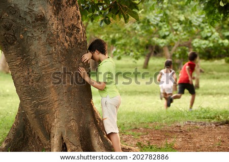 young boys and girls playing hide and seek in park, with kid counting leaning on tree Royalty-Free Stock Photo #202782886