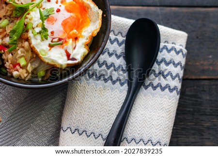 Japanese-style fried rice served in a black bowl with a fried egg and red tomato slices.