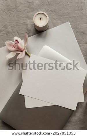 Aesthetic luxury bohemian minimalist concept. Blank clipping path paper sheet invitation card, laptop computer, pink flower, candle on neutral linen cloth. Flat lay, top view