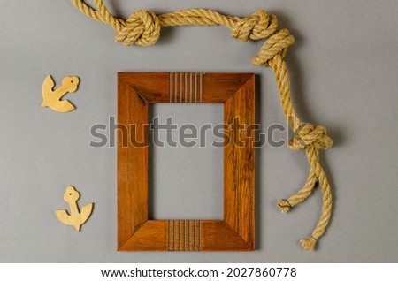 Empty photo frame and rope against a gray background. Wooden picture frame. Natural rope. Wooden anchors. Top view.