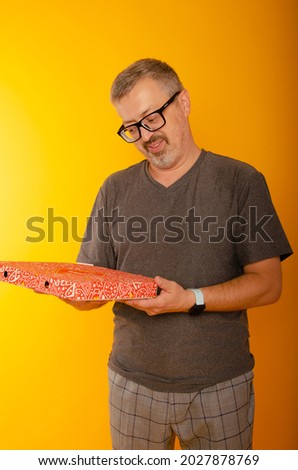 Image of happy optimistic emotional senior grey-haired bearded man posing isolated over yellow wall background holding pizza.