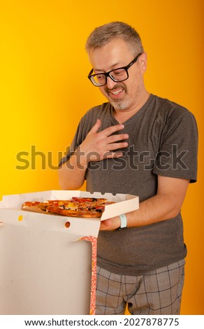 Image of happy optimistic emotional senior grey-haired bearded man posing isolated over yellow wall background holding pizza.