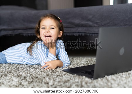 A little girl is talking very emotionally over a video link. The girl sits on the bed and watches cartoons or lessons. Distance learning via video communication.