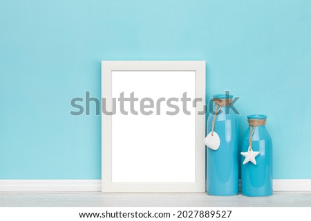 Vertical white picture frame with matte and two vases in front of turquoise wall. Elegant poster mockup. Blank image area isolated with clipping path.