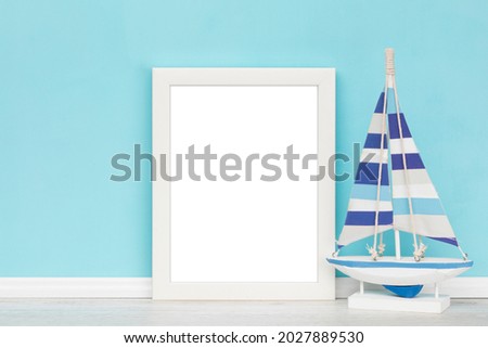 Vertical white picture frame with matte and decorative wooden sail boat in front of turquoise wall. Elegant poster mockup. Blank image area isolated with clipping path.