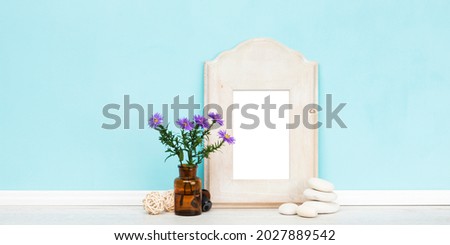 Vertical rustic wooden picture frame with matte and purple daisies in apothecary bottle in front of turquoise wall. Blank image area isolated with clipping path. Banner shaped  mockup. 