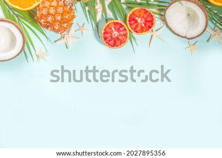 Summer vacation flat lay with with pineapple coconut orange fruit, palm leaves and sea shell, over light blue background copy space top view
