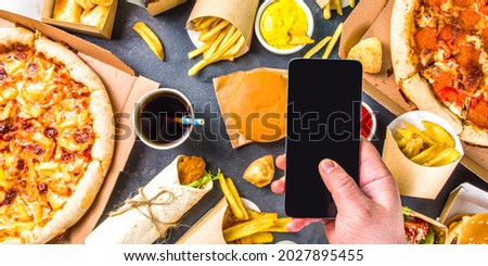 Delivery fastfood ordering food online concept. Large set of assorted take out foods, mans hands with smartphone in pic flatlay rop view
