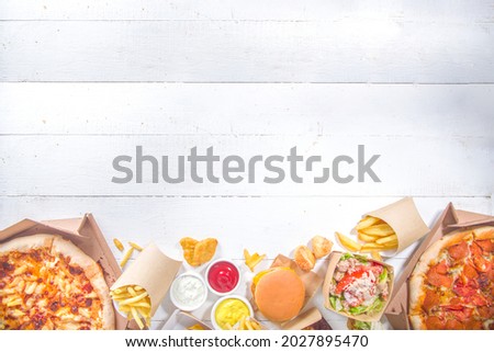 Delivery fastfood ordering food online concept. Large set of assorted take out foods pizza, french fries, fried chicken nuggets, burgers, salads, chicken wings, various sides, white table background  Royalty-Free Stock Photo #2027895470