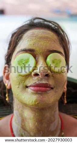 A beautiful woman with facial clay mask on face and fresh cucumber on eyes relaxing at Home. Portrait of beautiful spa girl. Beauty, healthcare. Multani Mitti and green Face Pack in India