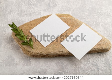 White paper business card, mockup with natural stone and boxwood branch on gray concrete background. Blank, side view, still life, copy space.