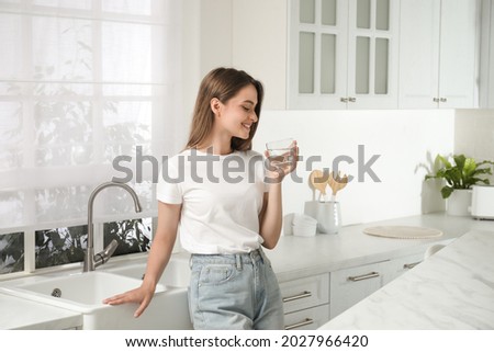 Woman drinking tap water from glass in kitchen Royalty-Free Stock Photo #2027966420