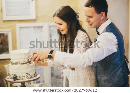 Stylish happy bride and groom cutting together modern cake with lavender on background of festive table in stylish restaurant. Provence wedding reception. Beautiful wedding couple celebrating