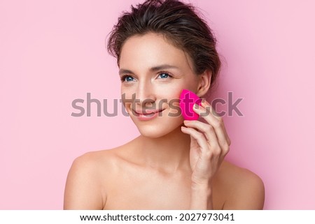 Woman applying foundation using cosmetic sponge, beauty blender. Photo of woman with perfect makeup on pink background. Beauty concept