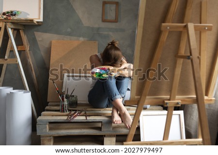 Depression in a woman artist, a young lady student sits in an art studio near an easel and canvas bowed her head and cries. Copy space.