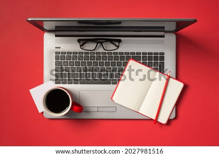 Top view photo of sticker note red cup of drink pencil on open red notepad and glasses on open grey laptop on isolated red background with blank space