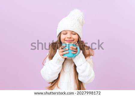 A little girl holds a cup with a warm drink in the cold season. Winter clothes on the child.