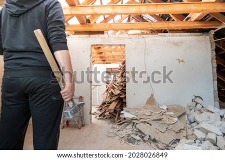 Construction worker with a sledge hammer after demolishing  a brick wall in a private home. Royalty-Free Stock Photo #2028026849