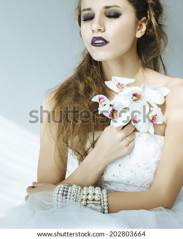 Bride in white dress with pearl bracelets with orchid flower in her hand, silhouette 