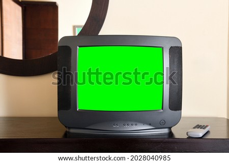 An old black TV with a green screen for adding video and images is on the bedside table in the apartment . Vintage TVs from the 1980s 1990s 2000s. 