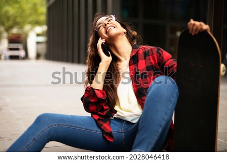 Portrait of young beautiful girl with skateboard. Happy smiling girl talking to the phone	