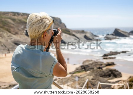 Woman taking a photo of beautiful rocky beach in Zambujeira do Mar, Portugal