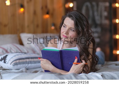 lifestyle soft image of pretty young woman sitting on her cozy bed and making notes to her diary. Fall season mood.