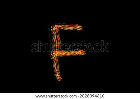 Letter F. Light painting alphabet. Long exposure photography. Drawing letter F with colorful lights on black background.