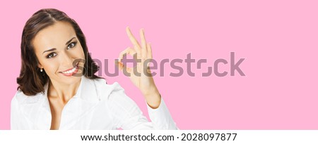 Businesswoman in white confident clothing showing ok hand sign gesture, rose pink color background. Portrait of happy smiling gesturing brunette woman at studio. Business ad concept. Female manager.