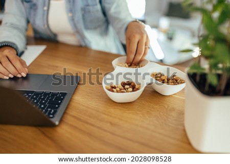 Healthy eating and working. Woman eating nuts while working on laptop. Close-up. Royalty-Free Stock Photo #2028098528