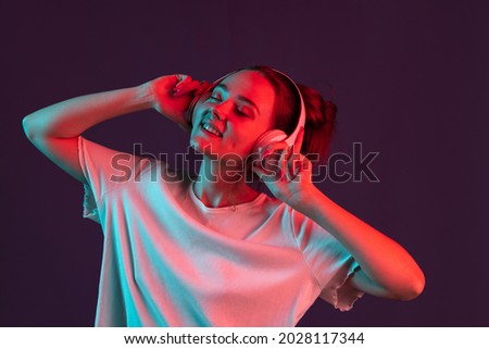 Musician. Portrait of sweet, pretty girl on dark purple studio background in red neon light, filter Concept of human emotions, facial expression, beauty, sales. Copy space for ad. Listening to music