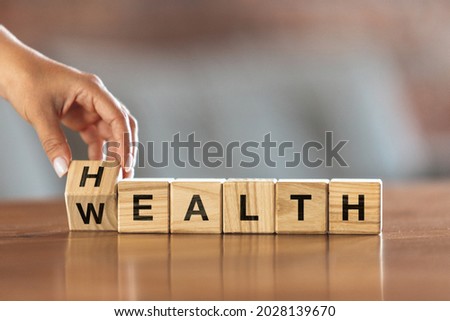 Wealth. Female hand turning one wooden cube, block and change sense of word. Conceptual image about human rights, social issues, mental health, education and personal development. Right choice Royalty-Free Stock Photo #2028139670