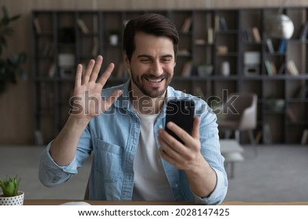 Happy millennial man looking at cellphone screen, enjoying pleasant distant web camera call using mobile zoom video call application, communicating remotely with friends or family, sharing life news. Royalty-Free Stock Photo #2028147425