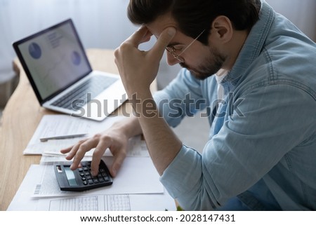 Frustrated depressed stressed young man calculating domestic expenses, having financial problems, considering bank debt, planning mortgage payments, feeling lack of money, bankruptcy concept. Royalty-Free Stock Photo #2028147431