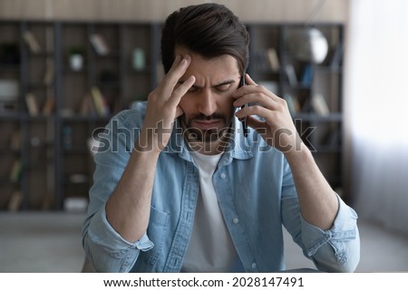 Stressed young man holding cellphone conversation, feeling displeased with bad negative news. Unhappy nervous male client dissatisfied with failure, listening debt notification, bankruptcy concept. Royalty-Free Stock Photo #2028147491