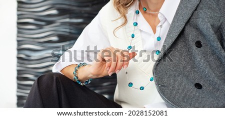 Women's fashion accessories. Beads and a bracelet made of blue stones. Business style of clothing and jewelry. A fragment of an elegantly dressed woman in a white shirt, and a white warm vest. Royalty-Free Stock Photo #2028152081