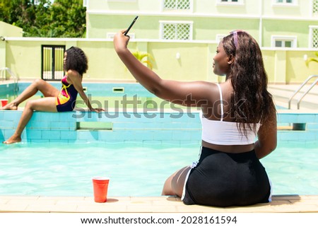 young attractive african woman taking selfies with her phone by the side of a pool
