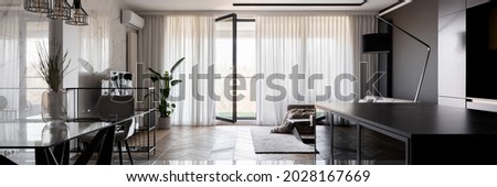 Panorama of spacious and open plan apartment with modern dining table,black kitchen and elegant living room with window wall behind curtains and balcony doors open Royalty-Free Stock Photo #2028167669