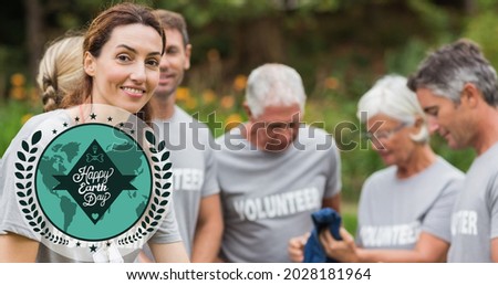 Composition of green globe logo and earth day text over volunteers cleaning up countryside. global conservation and earth day concept digitally generated image.