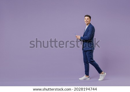 Full size young successful employee business man lawyer 20s wear formal blue suit white t-shirt work in office move stroll hold use mobile cell phone isolated pastel purple background studio portrait