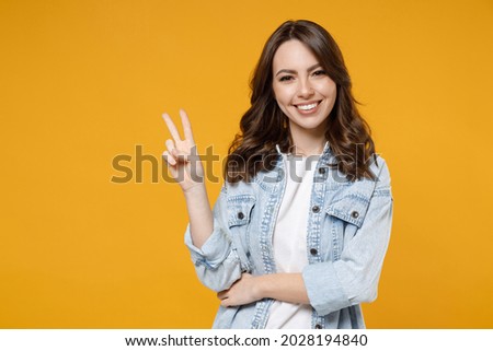 Young caucasian smiling happy brunette friendly woman 20s in stylish casual denim shirt white t-shirt show victory v-sign gesture isolated on yellow background studio portrait People lifestyle concept