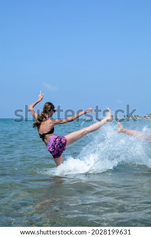 Cheerful smiling girl in sunglasses and bikini splashes in the sea against the blue sky