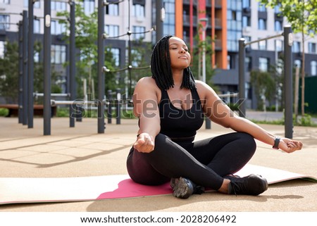 Side View On Black African Lady Meditating Outdoors, Keep Calm, Engaged In Yoga Alone, Keep Calm And Balance, In Black Sportive Outfit. Copy Space. Obese Female Lead Healthy Lifestyle.