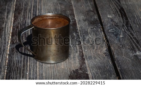Cup of coffee in a metal mug on a gray-brown wooden surface, light shadow, sunlight of morning coffee. Top view. Fragrant coffee in the morning	